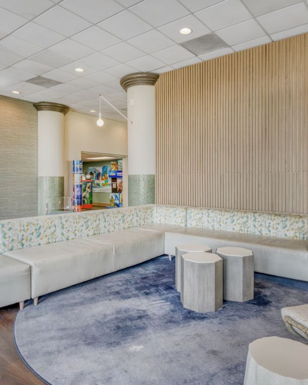 A modern lounge area with a curved sofa, round tables, chairs, and a circular rug, set against a backdrop of decorative columns.