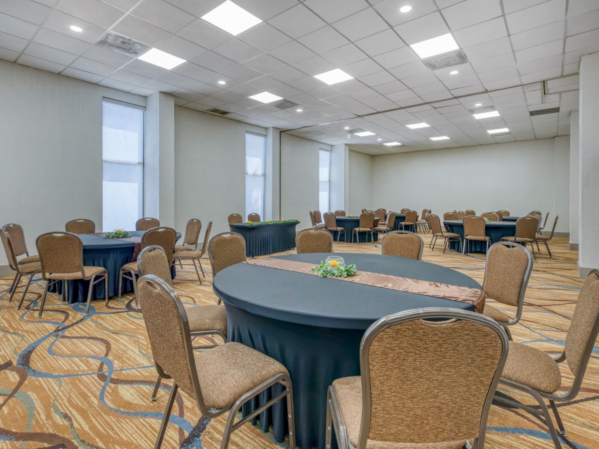A conference room with round tables and chairs arranged for an event, featuring a patterned carpet and a white ceiling.