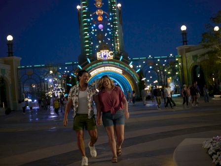 A couple walks in front of an illuminated entrance with "Epic" written above, set against a nighttime backdrop filled with lights.