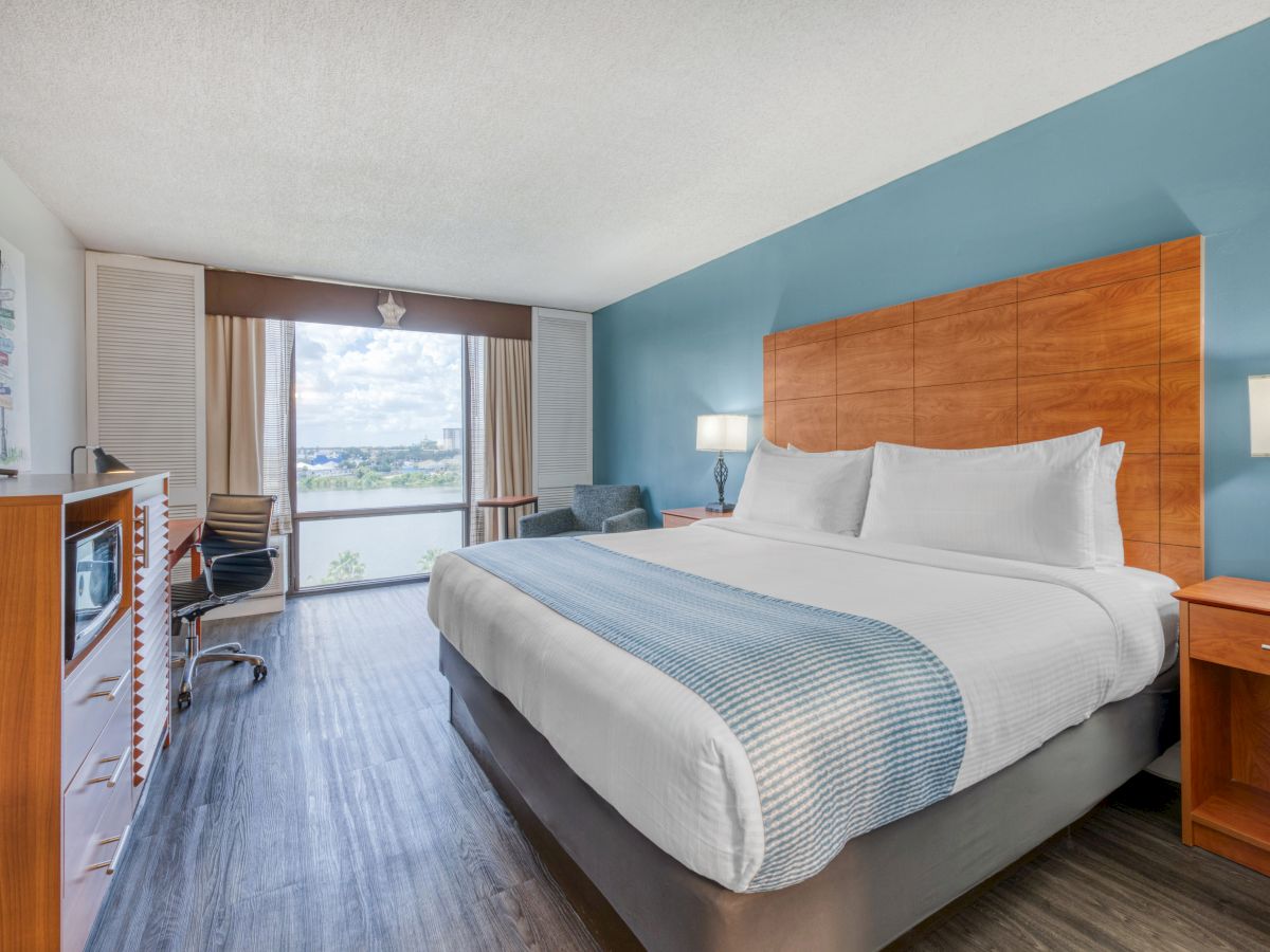 A modern hotel room with a large bed, blue accent wall, flat-screen TV, and window view.
