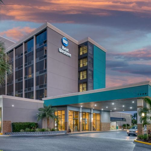 The image shows a Best Western hotel with a modern entrance, palm trees nearby, and a warm sunset in the sky.
