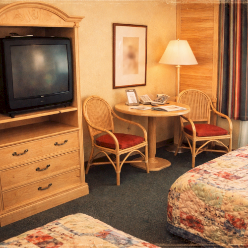 A hotel room with a TV, microwave, small table with chairs, lamp, and two beds with patterned bedspreads.