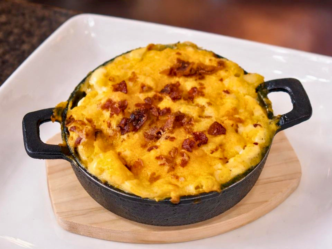 A dish of baked mac and cheese in a small, round cast iron pan, topped with melted cheese and breadcrumbs.