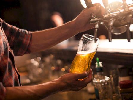 Someone is pouring a glass of beer from a tap at a bar or pub, with a warm, dimly lit atmosphere.