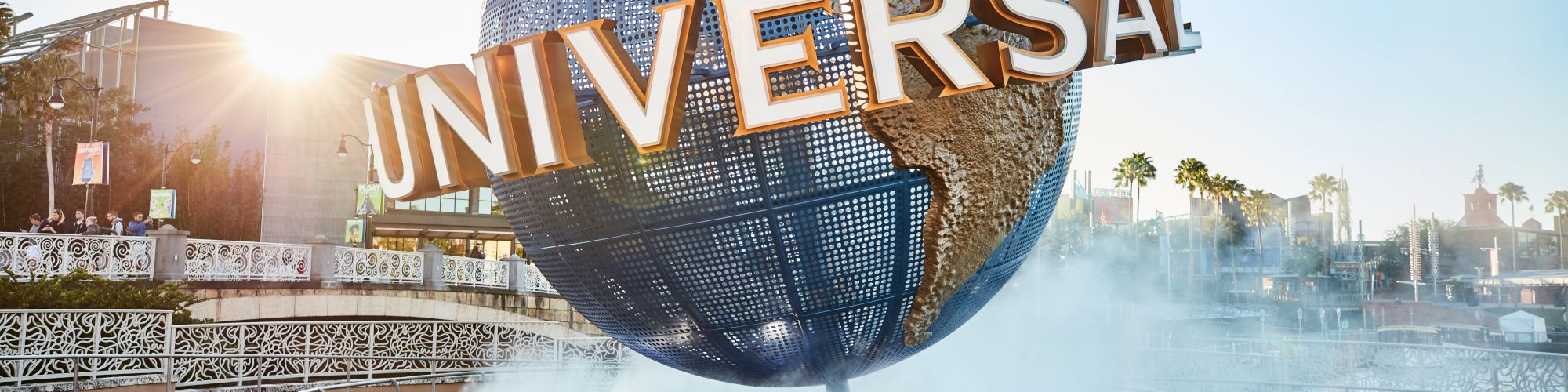 A large globe structure with "Universal" written on it, surrounded by mist and a fountain, likely at Universal Studios theme park.