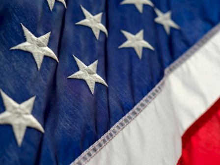 The image shows a close-up of the United States flag, displaying part of the blue field with white stars and a portion of the red and white stripes.