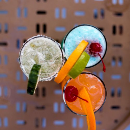 Three colorful cocktails topped with assorted garnishes including fruits and cherries.