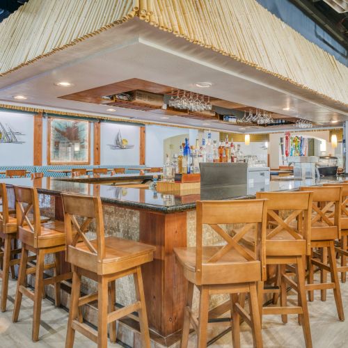 This image shows a bar area with wooden stools, a countertop, and hanging glasses under a decorative canopy.