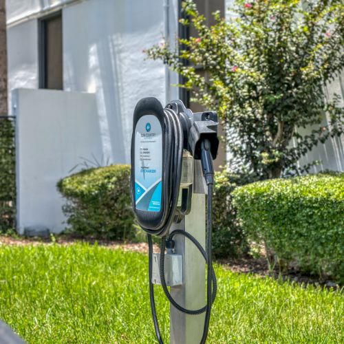 The image shows an electric vehicle charging station set in a grassy area near a building.