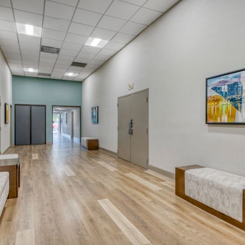 A long hallway with benches and framed artwork on the walls, featuring wood flooring and ceiling lights.