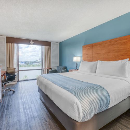 A hotel room with a large bed, TV, desk, and window view. It has modern decor with blue and wood accents.