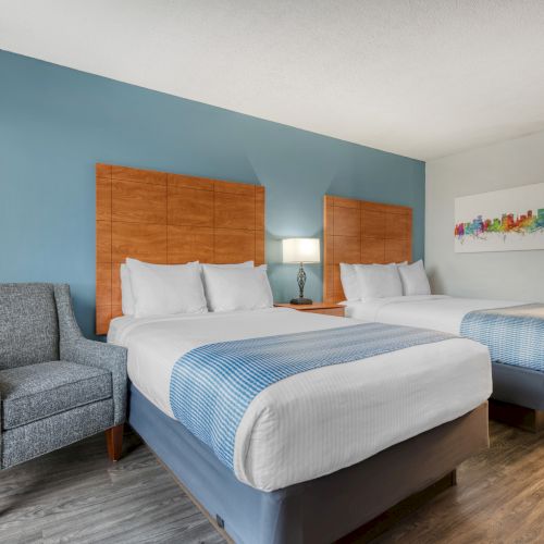 The image features a hotel room with two neatly made beds, an armchair, a side table, and a colorful artwork on the wall.