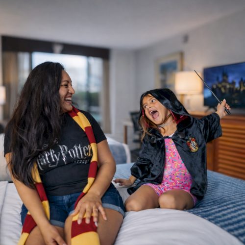 A woman and a child in a hotel room wear themed outfits, with the child holding a wand enthusiastically.