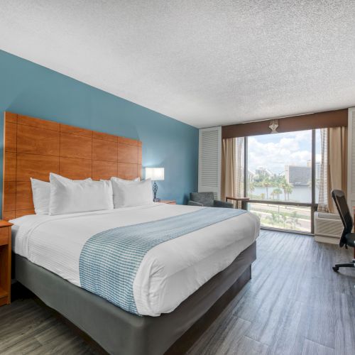 A hotel room with a large bed, blue accent wall, nightstands, lamps, a desk, and a window with a view.